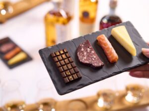 Chocolate, venison salami, salmon and smoked cheese canapes with whisky bottles in the background.
