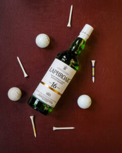 A bottle of Laphroaig 16yo. Pictured on a maroon leather background with gold balls and tees.