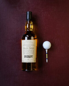 A bottle of Glen Spey Flora and Fauna. Pictured on a maroon leather background with gold balls and tees.