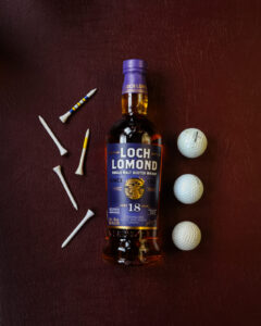 A bottle of Loch Lomond 18yo edition. Pictured on a maroon leather background with gold balls and tees.