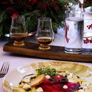 A dish of cured trout pictured with a whisky flight in a festive scene.