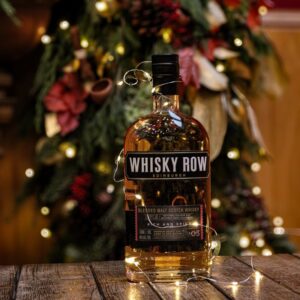 A bottle of Whisky Row - Rich & Spicy, set with a festive back ground and wrapped in fairy lights